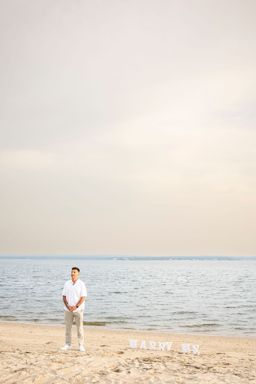 A serene beach scene with a person in white clothing walking along the sandy shore at sunset.