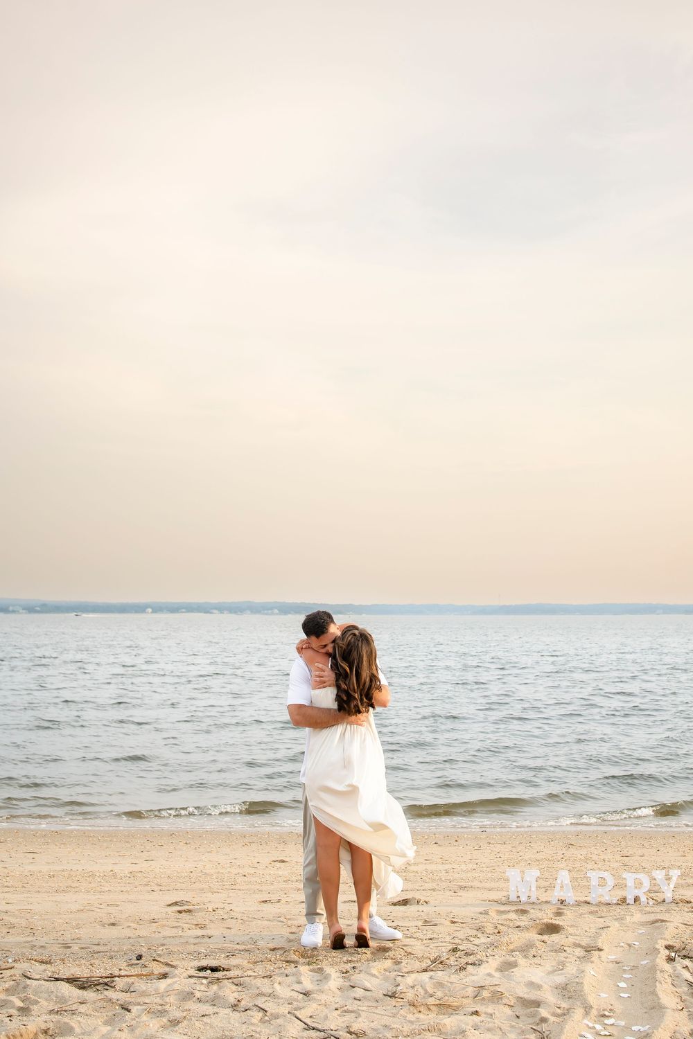 A romantic beach engagement moment with two people embracing on the sand at dusk.