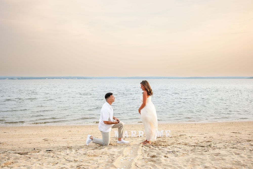 A romantic couple in white outfits walks along a serene beach at sunset during a photo session.