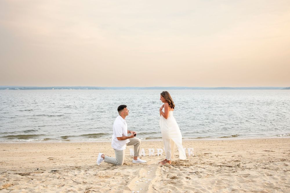 People in white outfits walk along a sandy beach at sunset with ocean waves in the background.
