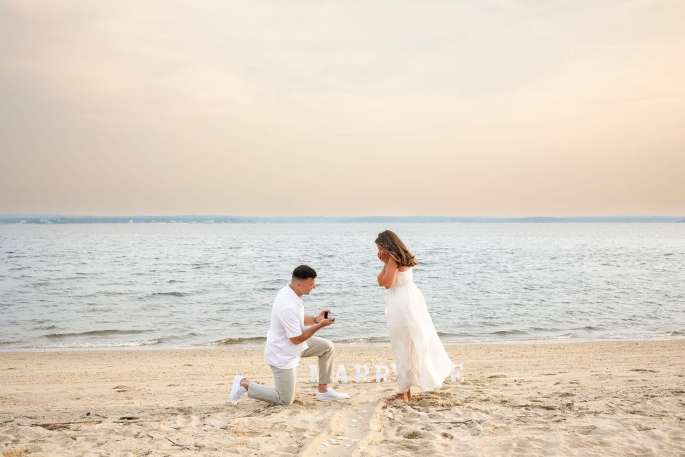 Two people in white outfits play together on a sandy beach at sunset near the ocean.