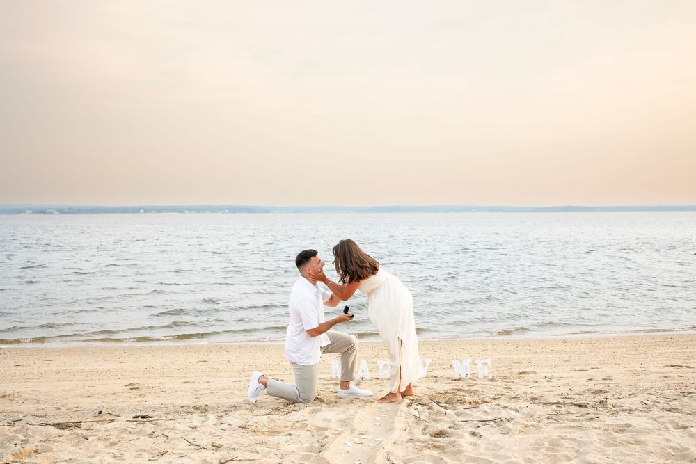 A romantic couple shares a tender moment on a sandy beach at sunset with ocean waves in the background.