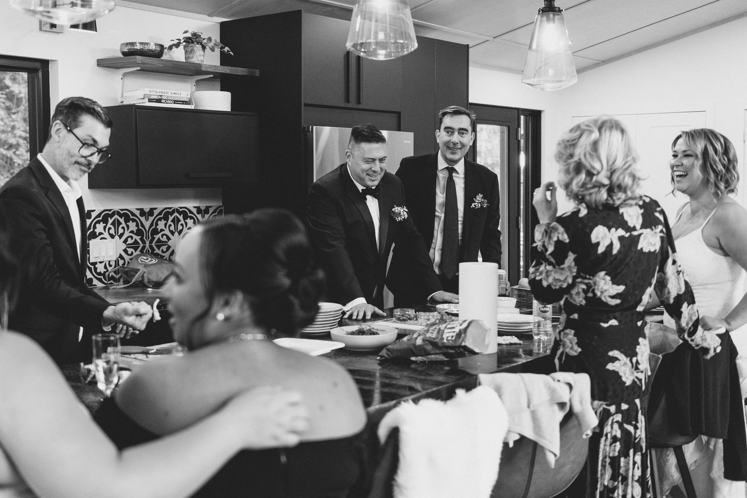 A group of people in formal attire gather around a table at an intimate indoor dining event in black and white photography.