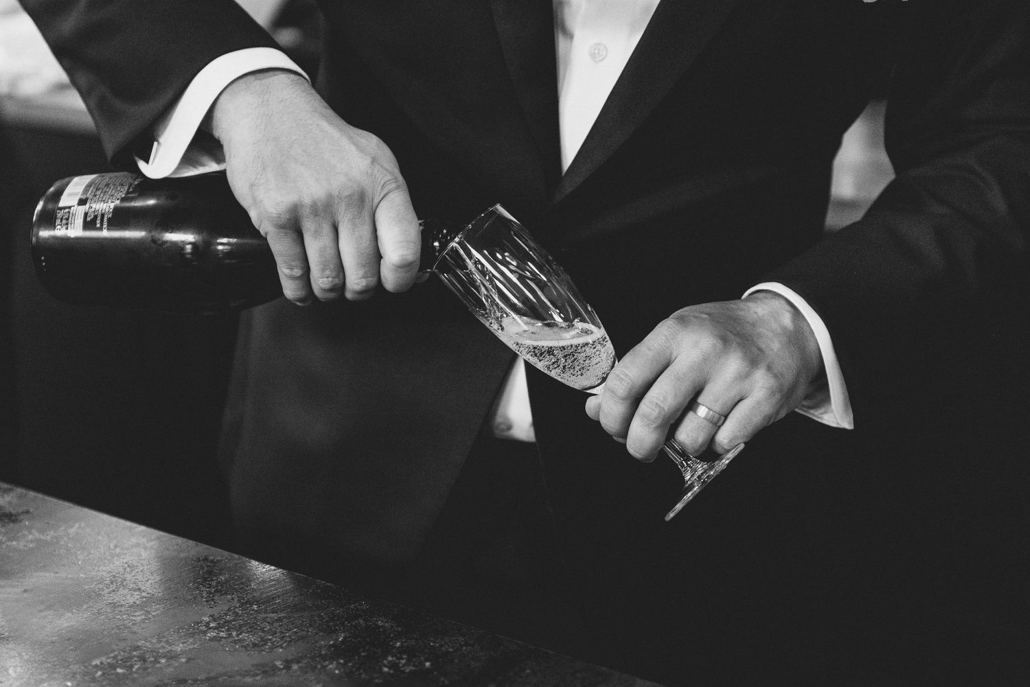 Black and white close-up of hands pouring champagne into a glass.