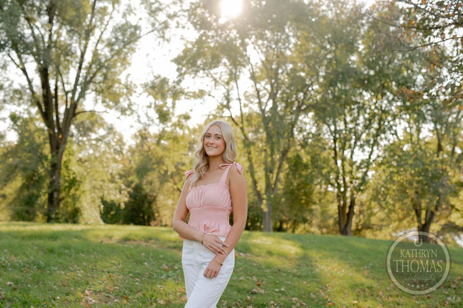 A pink top and white pants outfit photographed in a natural outdoor setting during golden hour.