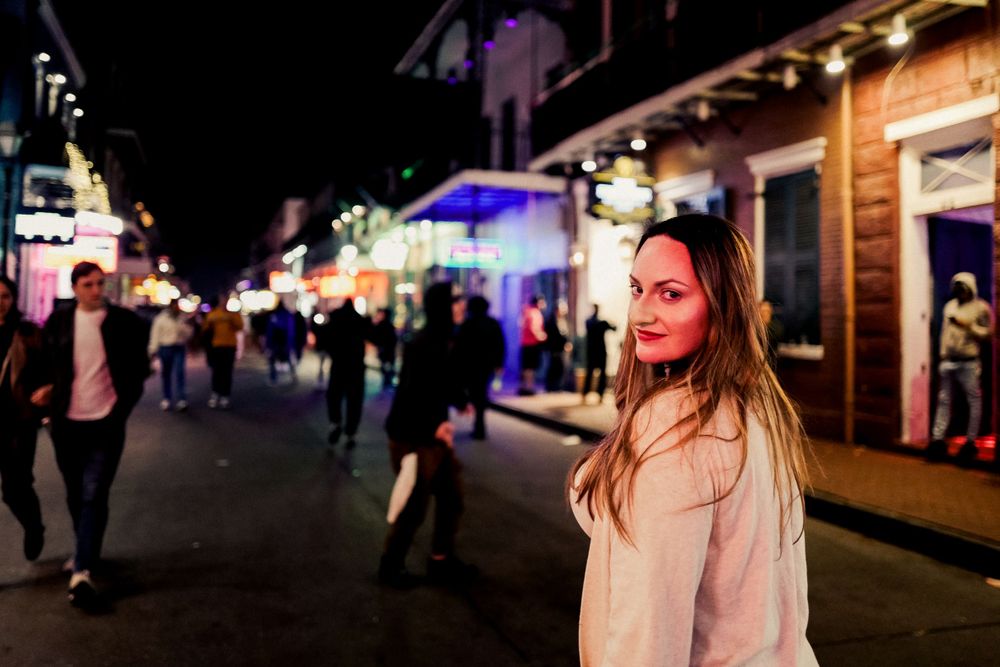 A person stands on a lively night street with pedestrians and illuminated storefronts on Bourbon Street in New Orleans.