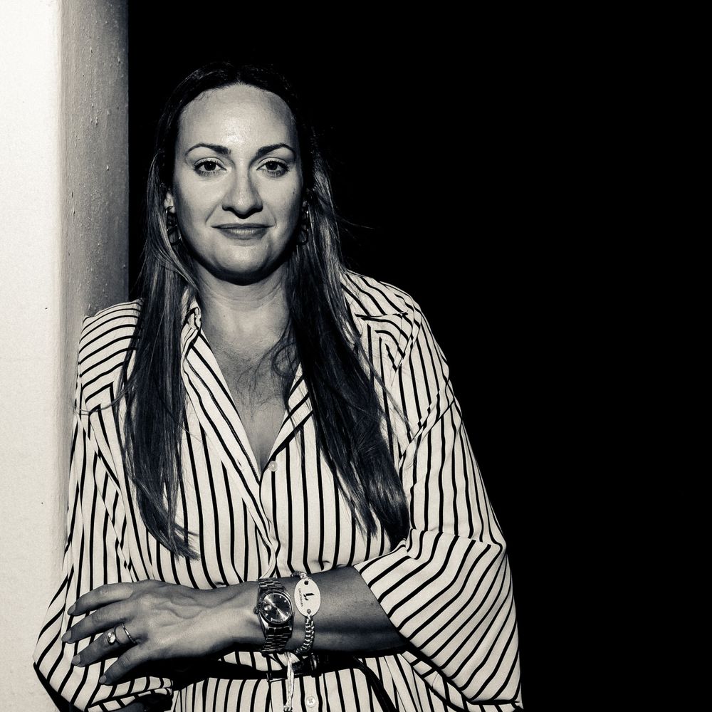 A professional black and white portrait of a person in a striped shirt with long dark hair posed against a simple background.
