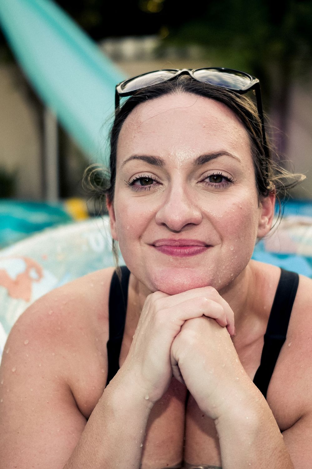 A relaxed portrait of someone wearing sunglasses on their head and a black tank top, resting their chin on clasped hands.