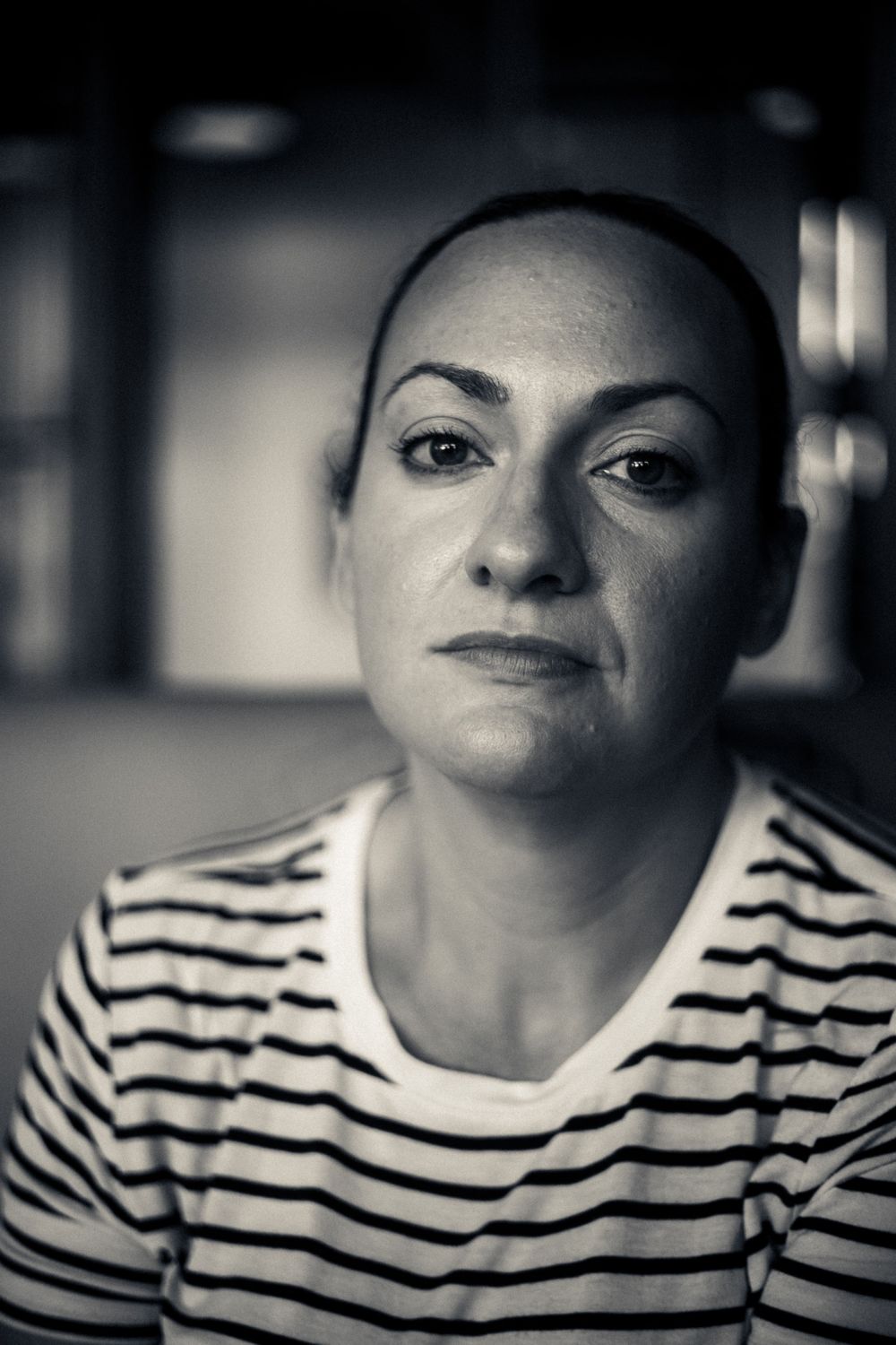 Black and white portrait of someone in a striped shirt with a contemplative expression against a dark background.