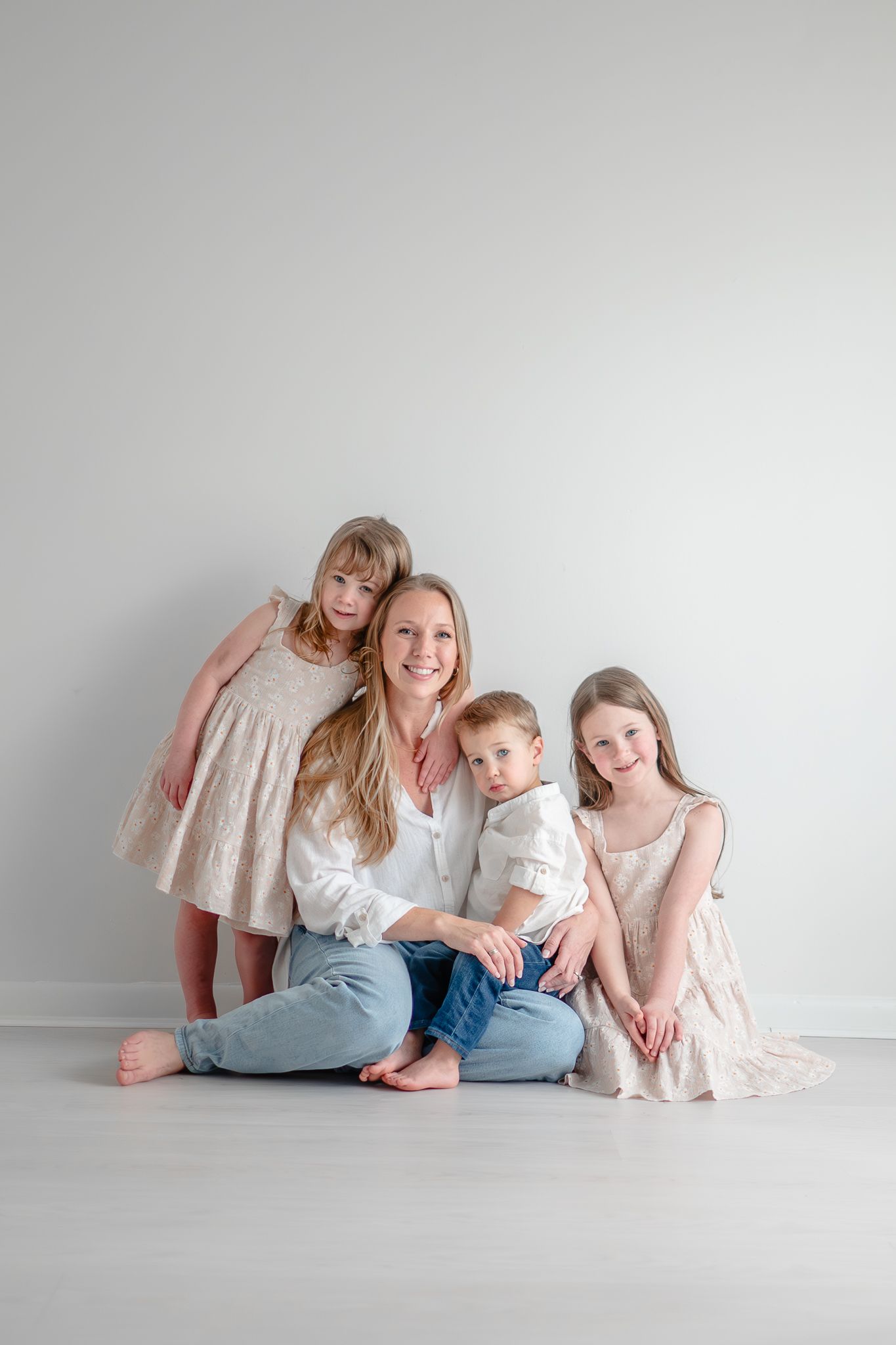 Family poses together in light neutral colored outfits against a white backdrop during indoor studio portrait session.
