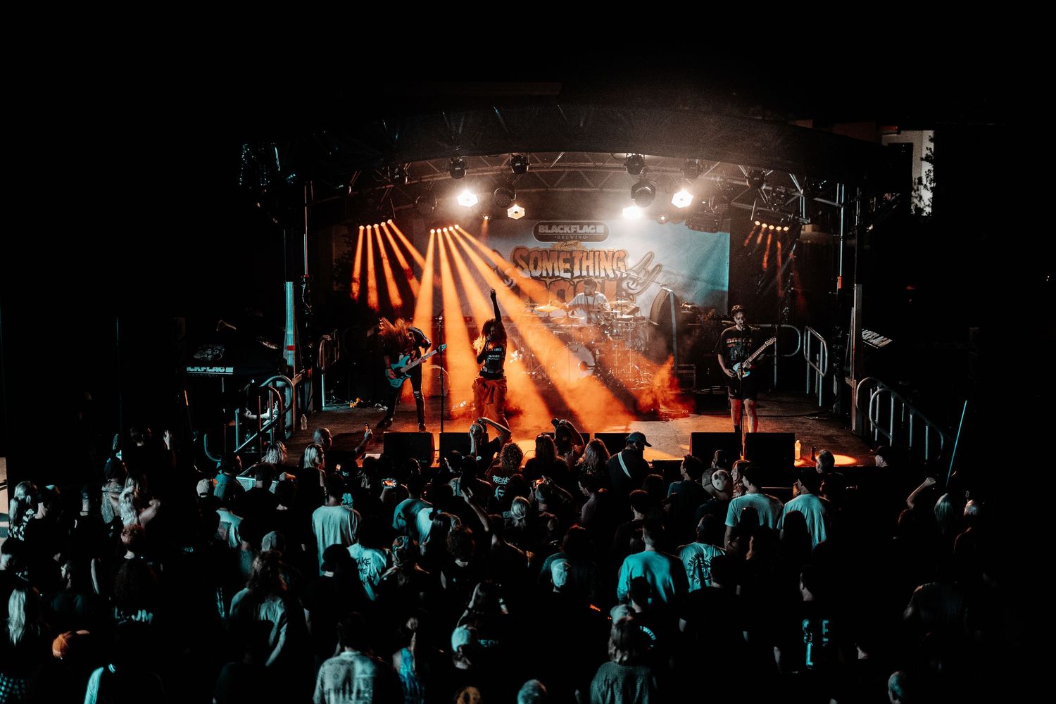 Concert venue filled with silhouetted crowd under dramatic orange stage lighting and fog effects.