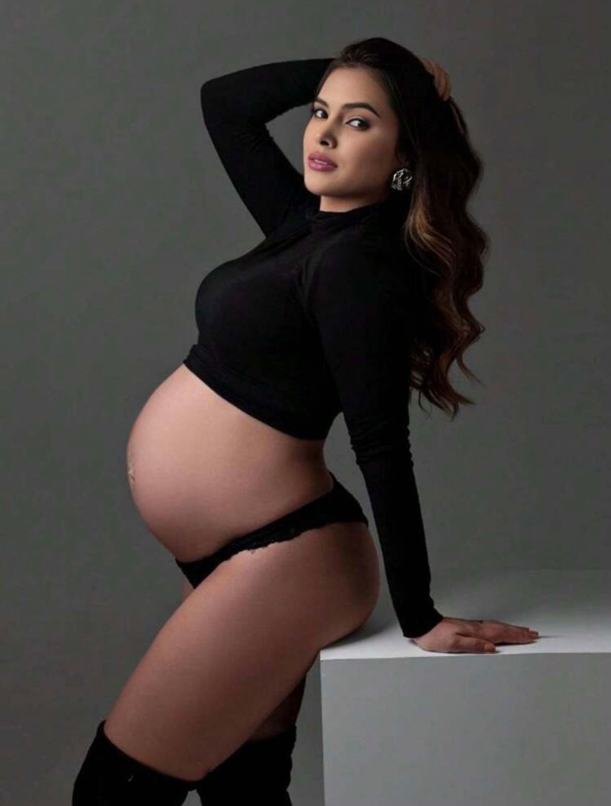 Dramatic maternity photo featuring woman in black outfit against dark background.