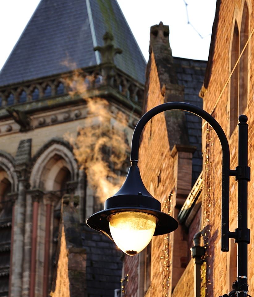 Vintage street lamp illuminated against gothic church architecture at dusk.