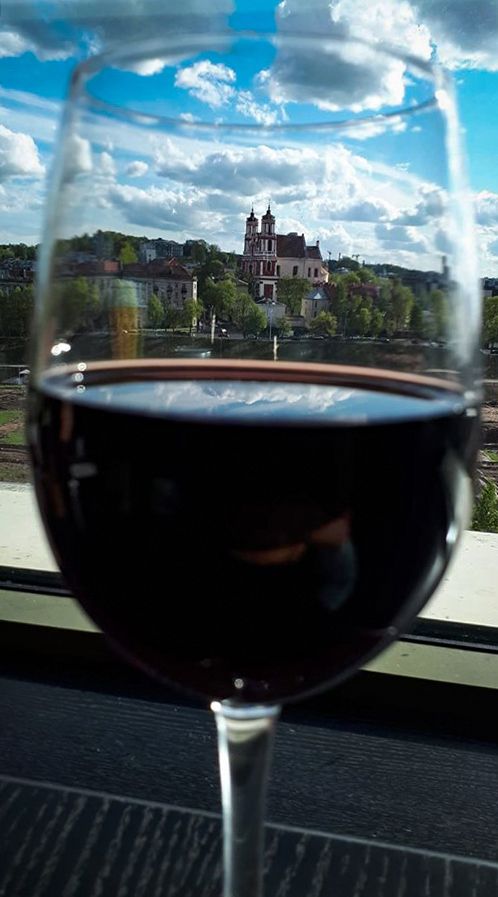 Glass of red wine overlooking a church through a window with blue sky and clouds.