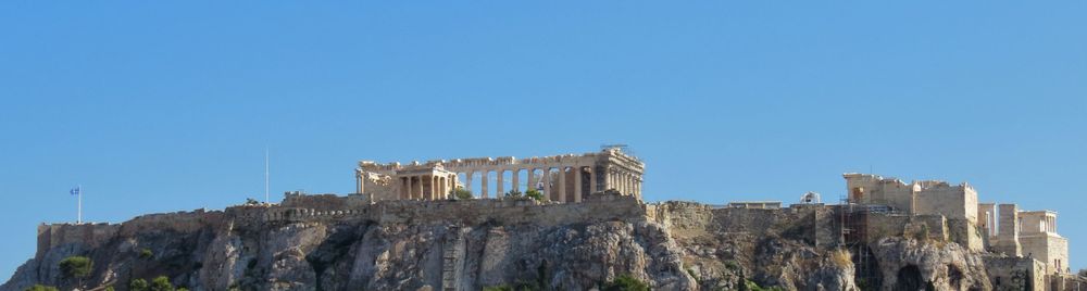 Ancient Acropolis ruins perched atop rocky hill against blue sky in Athens, Greece.