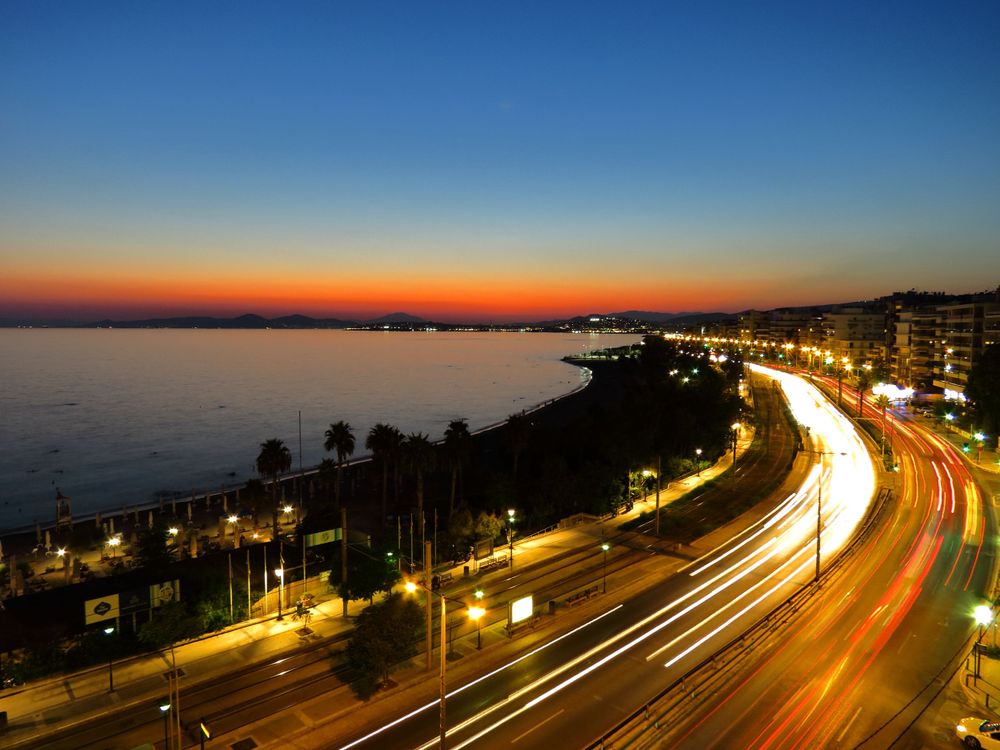 Coastal highway at twilight with light trails and illuminated buildings along curved shoreline.