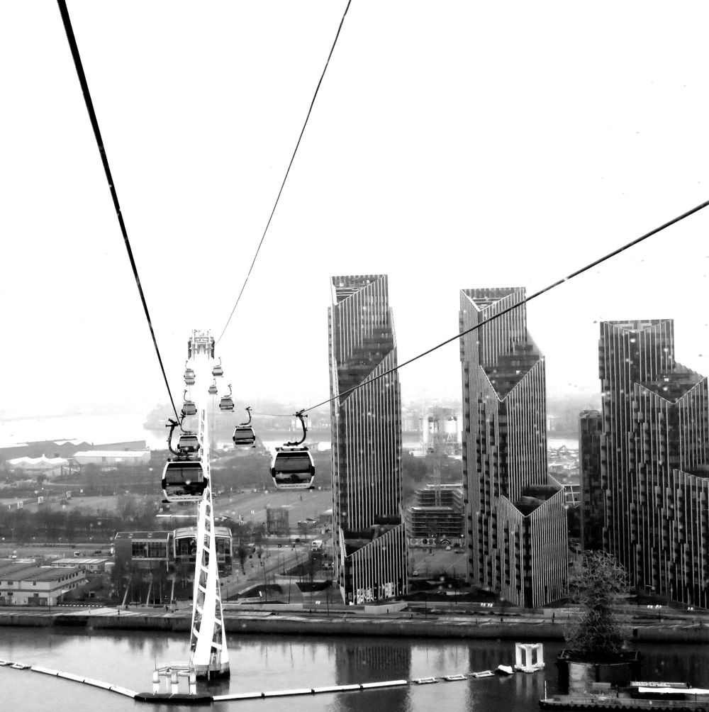 Cable car system crossing river with modern high-rise buildings in black and white cityscape.