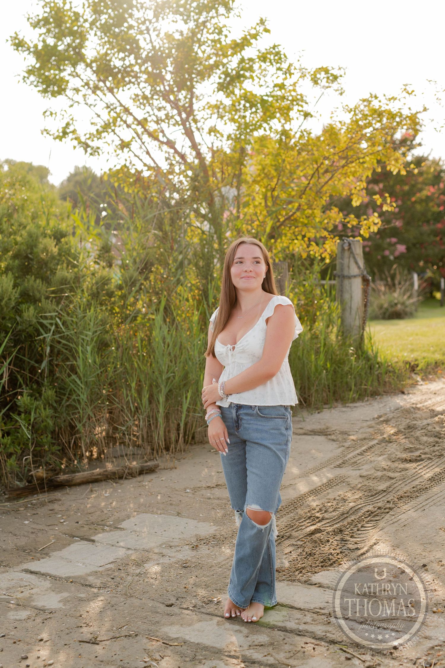 A casual outdoor portrait on a dirt path surrounded by tall grass and trees.