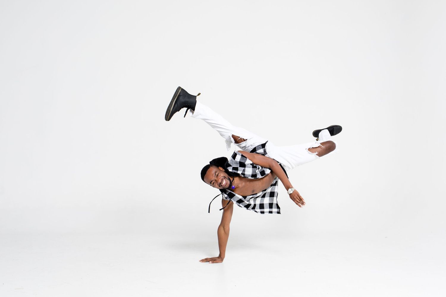 Dancer performing an energetic breakdance move against a white background, wearing a checkered shirt and black pants.