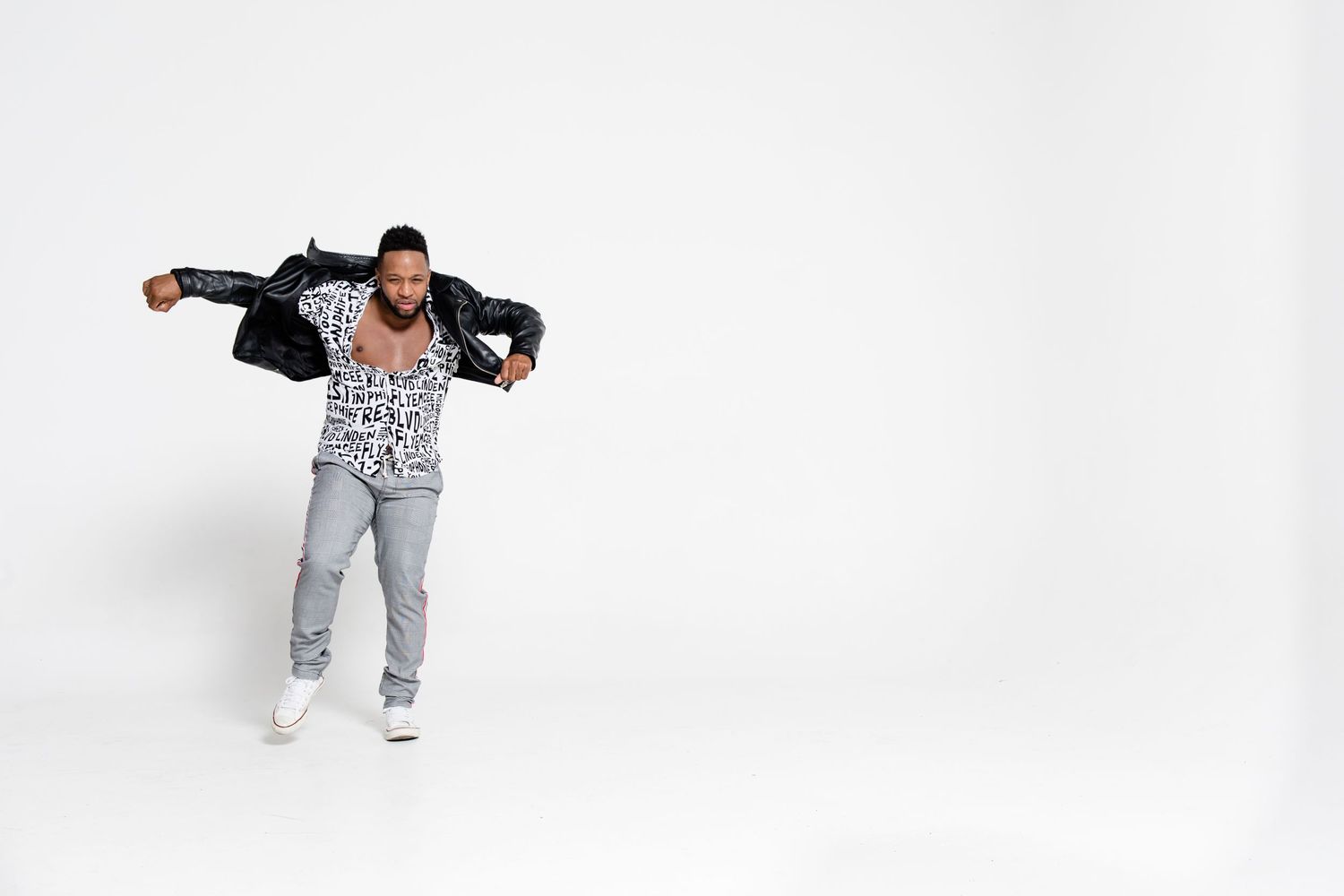 Someone dancing in a leopard print jumpsuit and black jacket against a white background.
