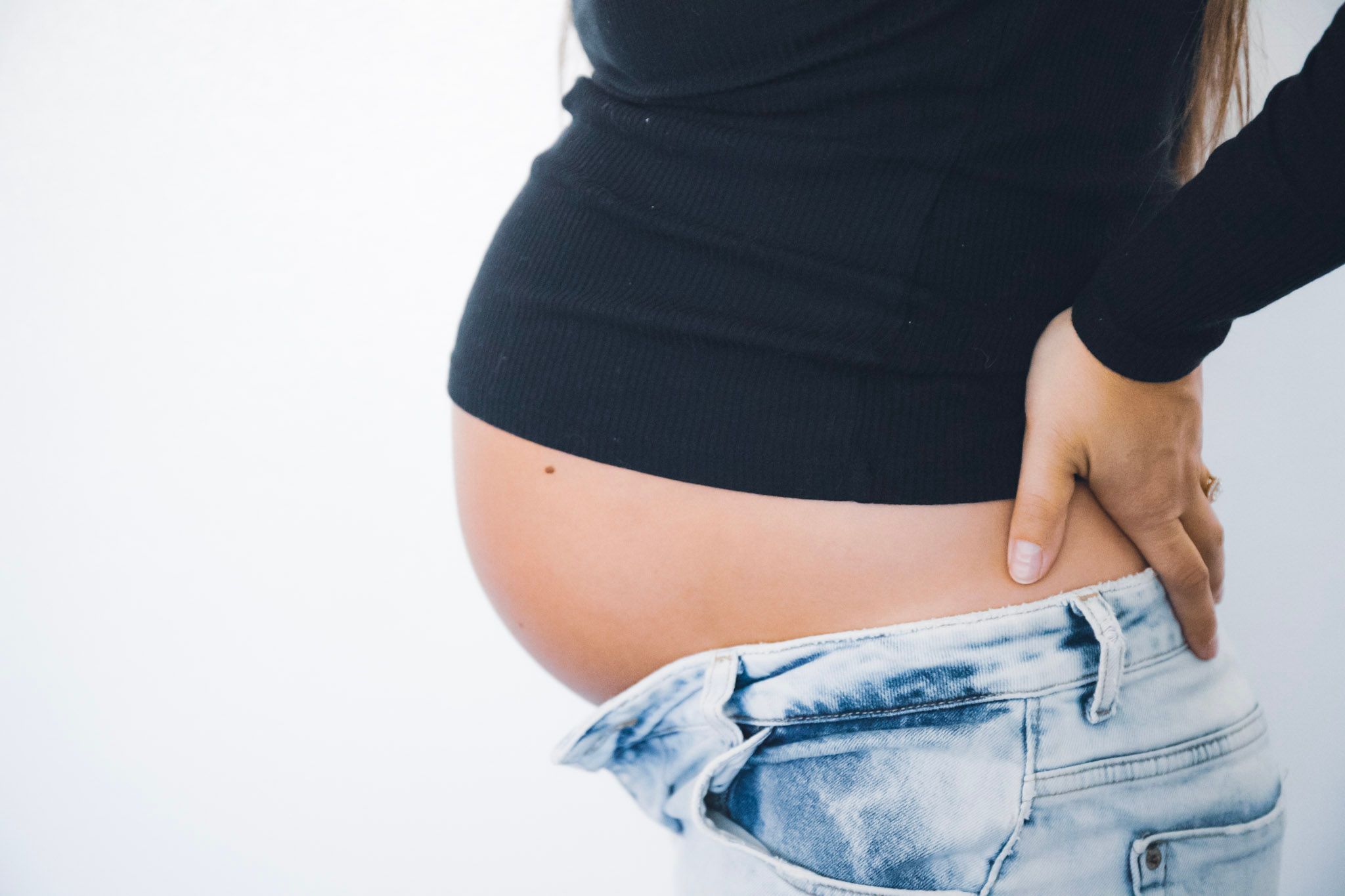 Side view of pregnant belly with black sweater and unbuttoned jeans.