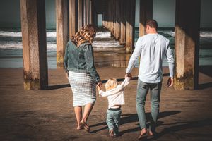 Family walking together under wooden pier at beach holding hands.