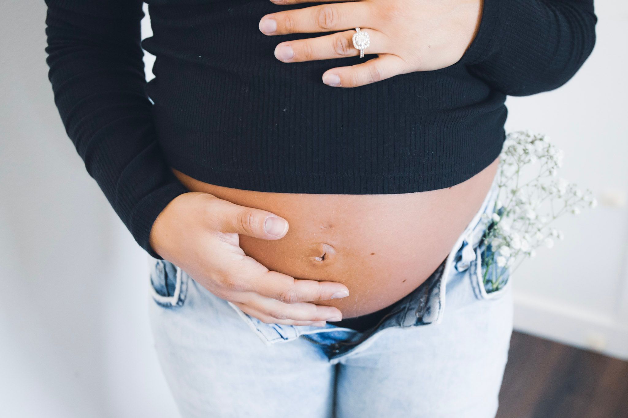 Close-up of pregnant belly with hands displaying engagement ring.