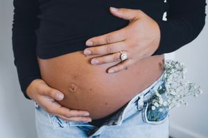 Maternity photo showing bare pregnant belly with hands forming heart shape.