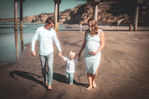 A family walks together holding hands on a beach with cliffs and pier in the background.