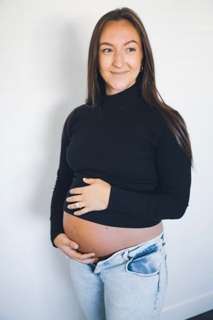 Maternity portrait of woman in black sweater showing baby bump.