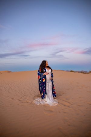 Ethereal maternity photoshoot featuring flowing dresses against desert sand dunes at sunset.