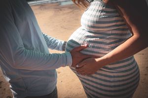Close-up of hands cradling a pregnant belly in a striped dress on a sandy beach.