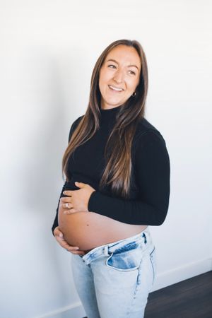 Joyful maternity portrait against white wall wearing black turtleneck.