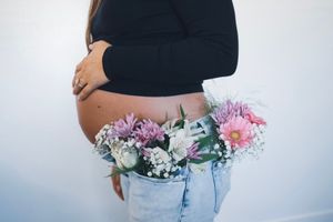 Artistic maternity photo with floral arrangement tucked in jeans waistband.