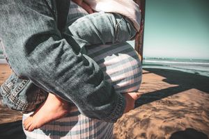 Close-up of child embracing pregnant belly on sandy beach.