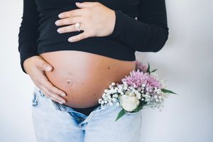 Maternity photo with pregnant belly and delicate pink and white flowers against white background.