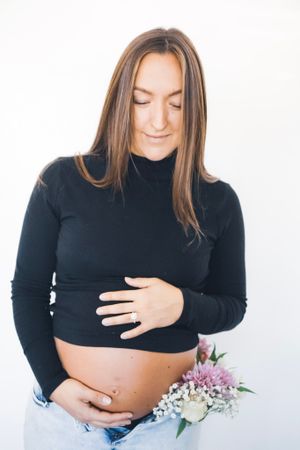 Expectant mother in black sweater holding belly with floral accents.