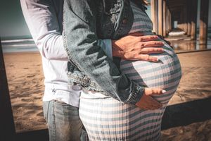 Close-up of hands cradling pregnant belly in striped dress at beach.