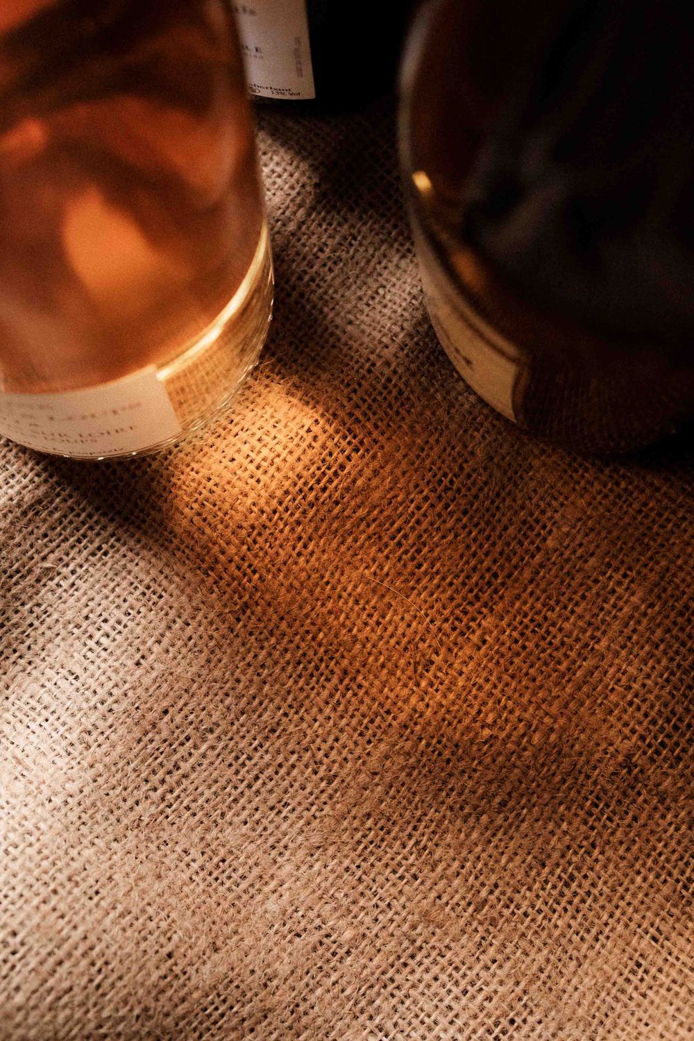Wine bottles on burlap fabric with warm lighting creating ambient shadows.