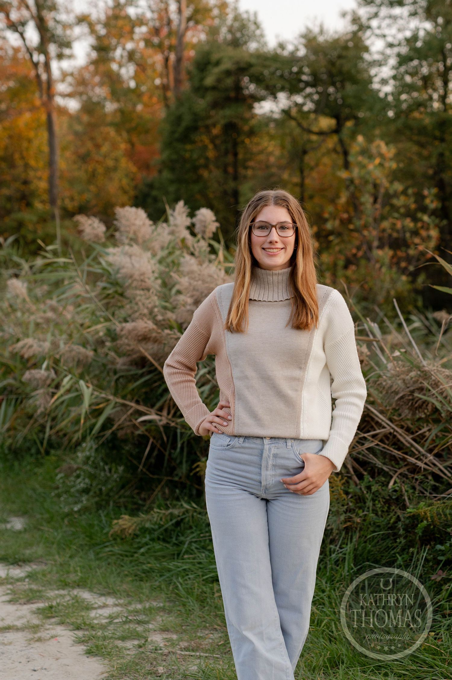 Standing portrait on nature path wearing two-tone sweater and jeans with autumn background.