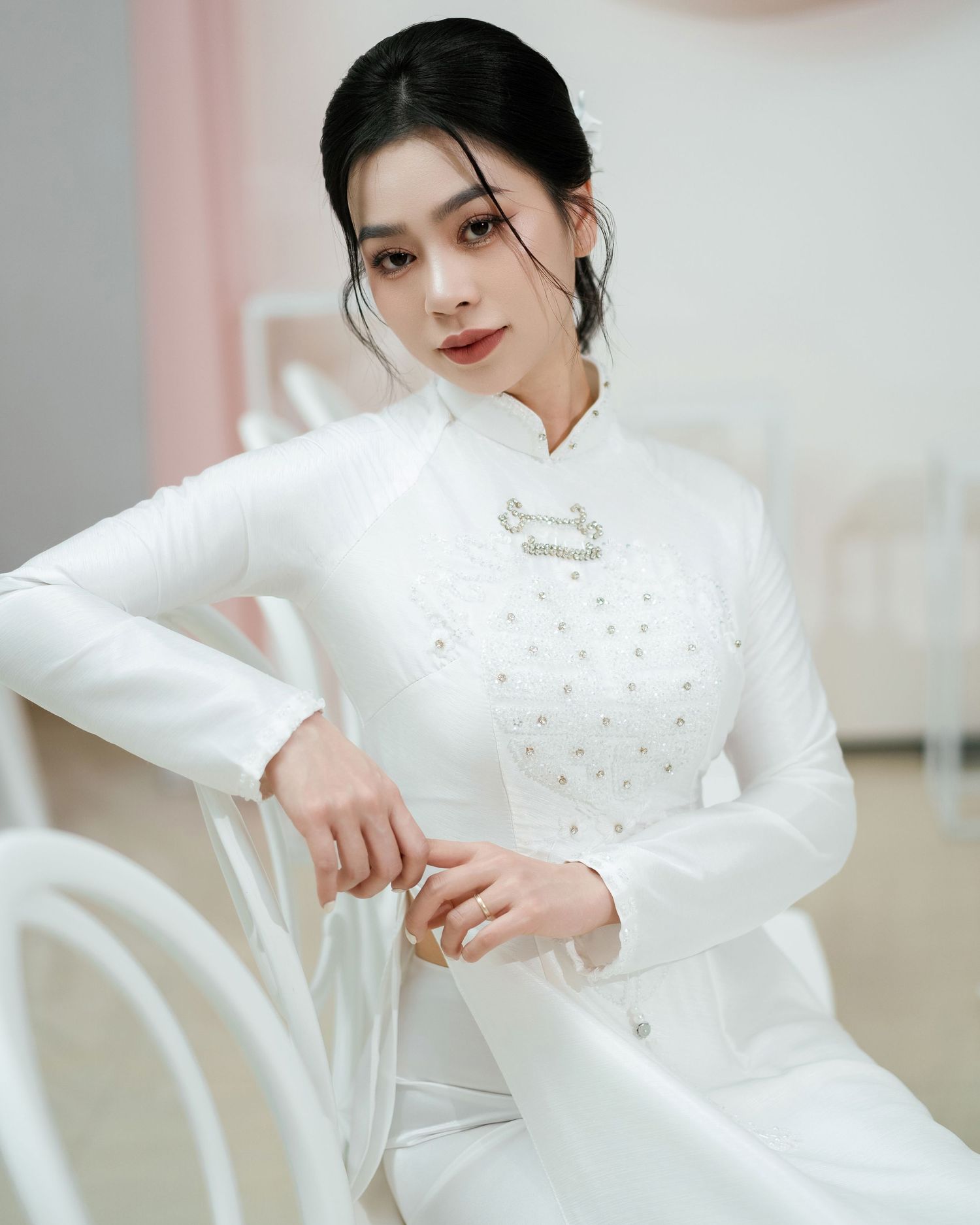 Traditional white Vietnamese ao dai dress with delicate floral embellishments photographed in an elegant indoor setting.
