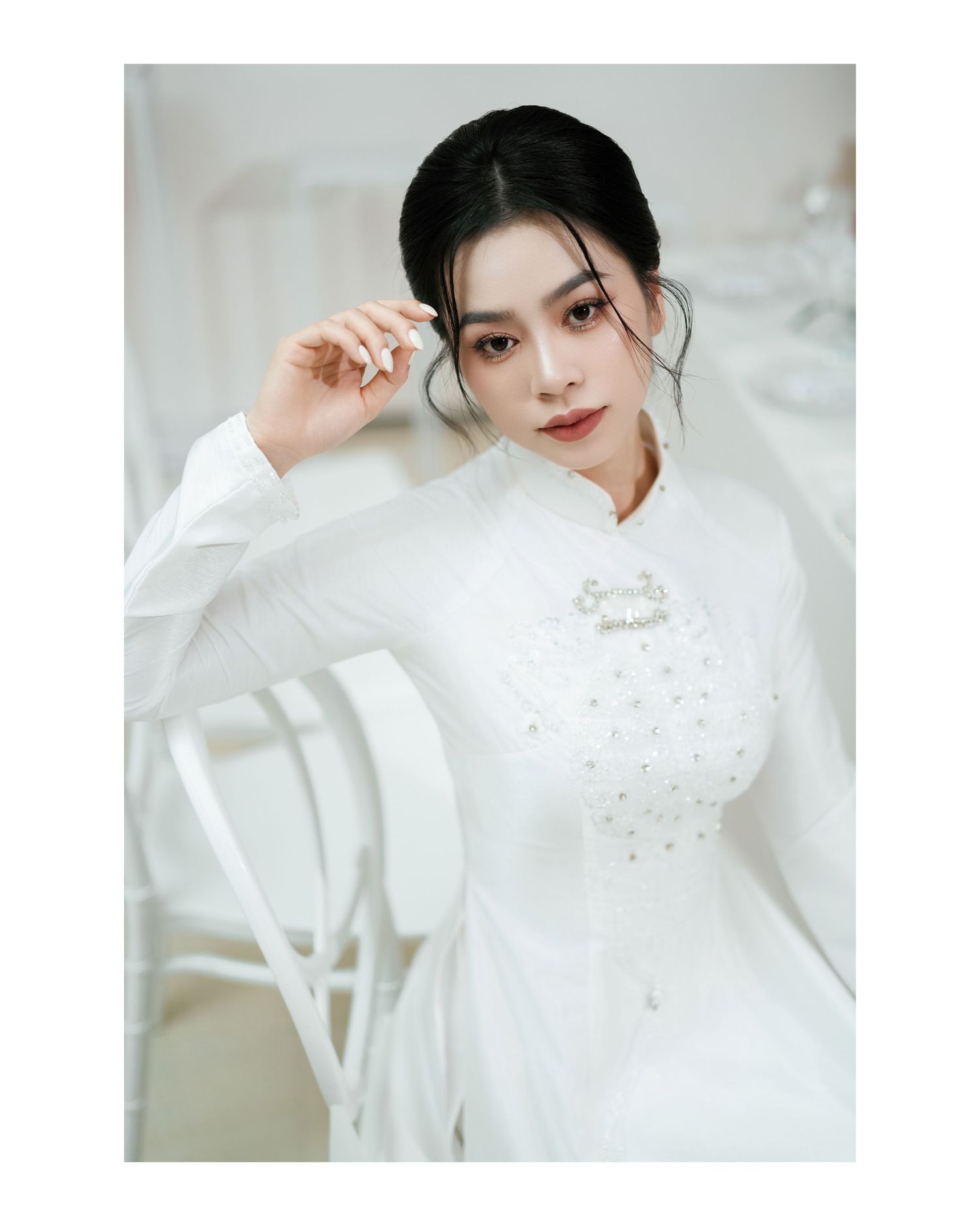 Elegant white ao dai dress with delicate floral embellishments in a light studio setting.