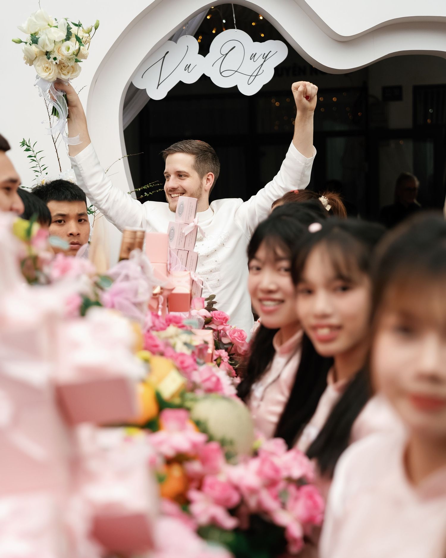 A joyful wedding celebration with guests surrounded by pink floral decorations and bouquets at a festive reception.