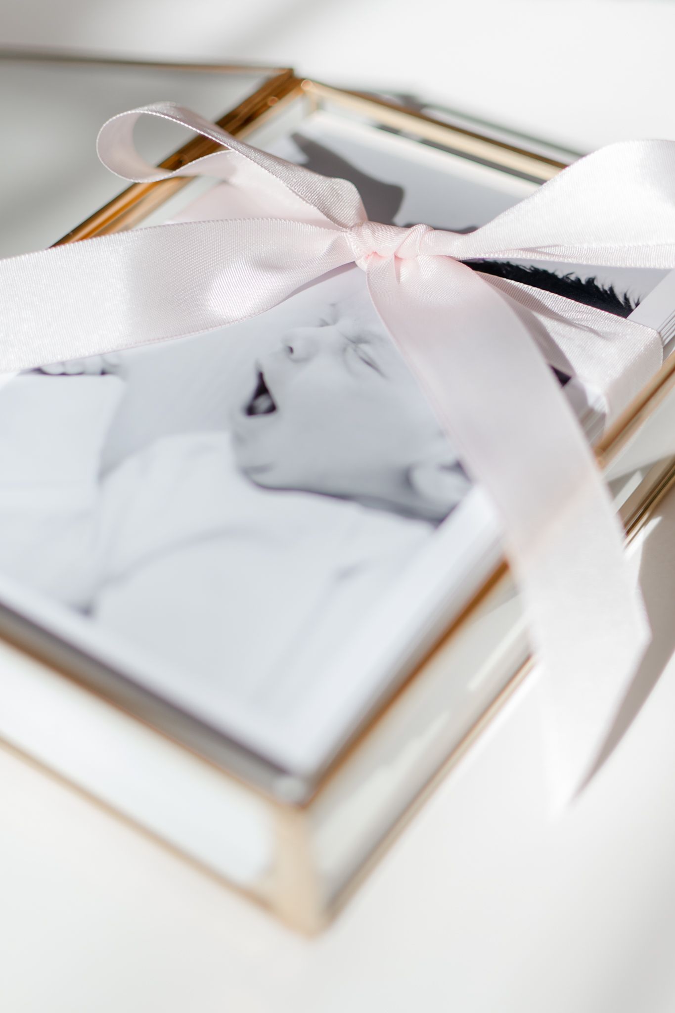 Black and white photo in an elegant frame tied with delicate pink ribbon bow on white surface.