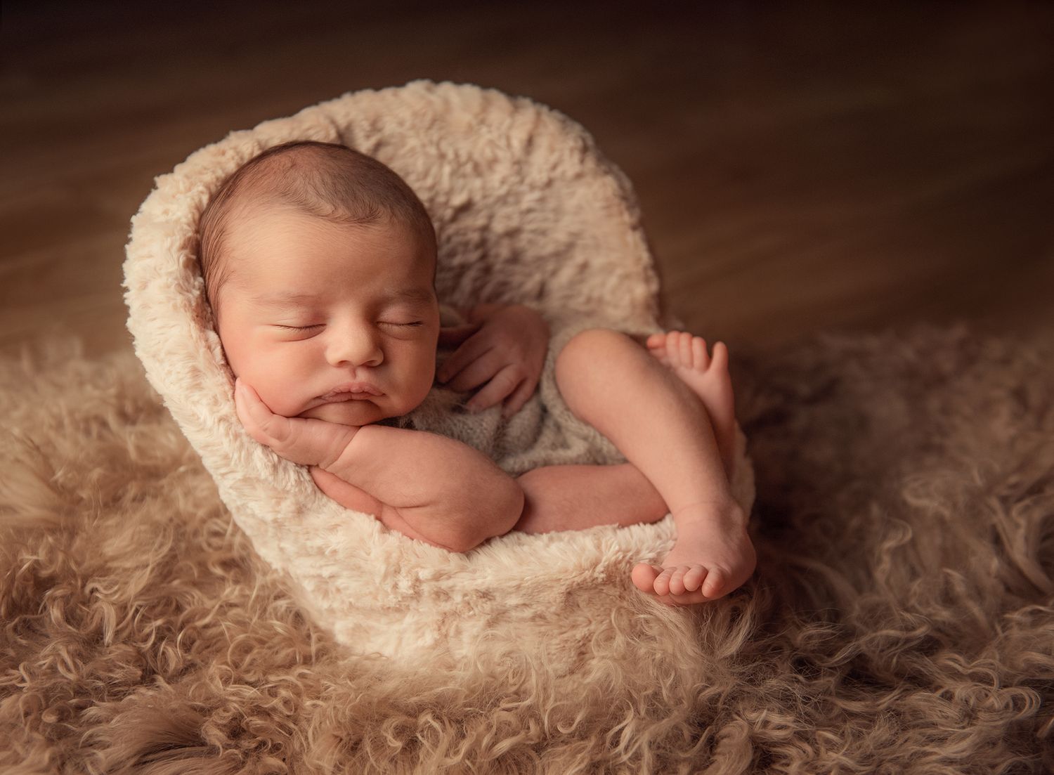 Peaceful sleeping newborn nestled in soft cream-coloured chair on brown textured backdrop.