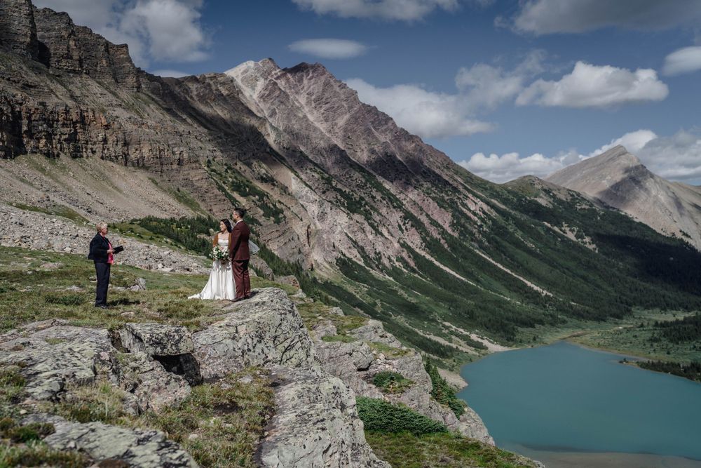 Couple stands at scenic mountain viewpoint overlooking turquoise alpine lake in dramatic Canadian Rockies landscape.