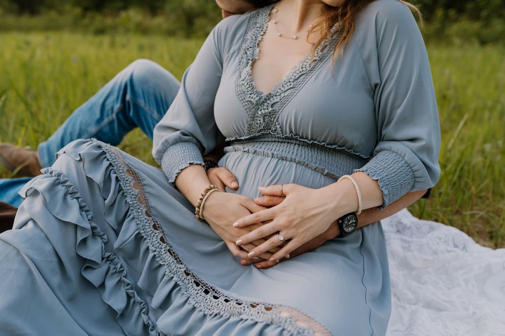 Pregnant mom sits on a blanket and holds her baby belly.