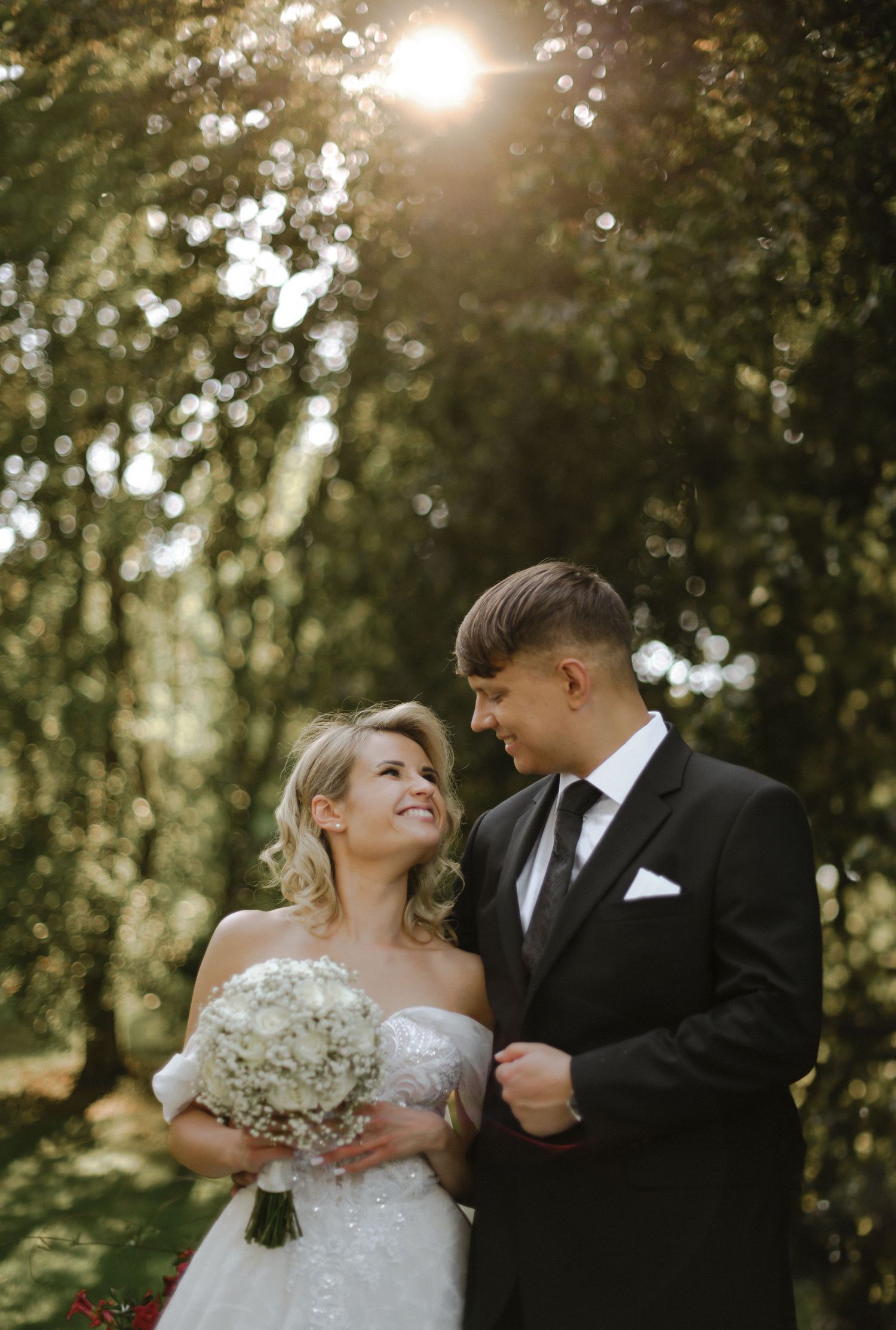Romantic wedding portrait with sunlit forest bokeh in background.