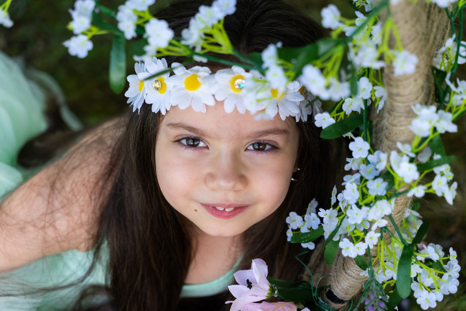 Child wearing a delicate crown of white daisies surrounded by spring flowers.