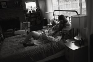 A moody black and white photograph of two people lounging together on a bed near a window. in Fort Wroth Texas.